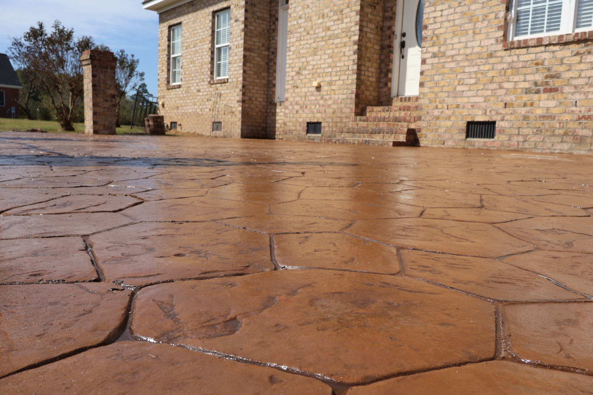 Warm-toned random stone stamped concrete in front of a brick house